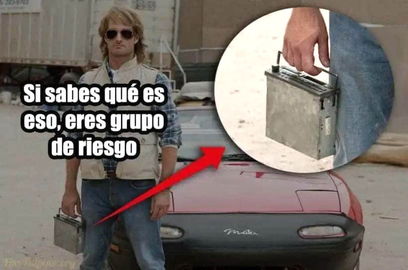 Hombre con gafas de sol y chaleco junto a un coche rojo, con un radiocasete extraíble en la mano.