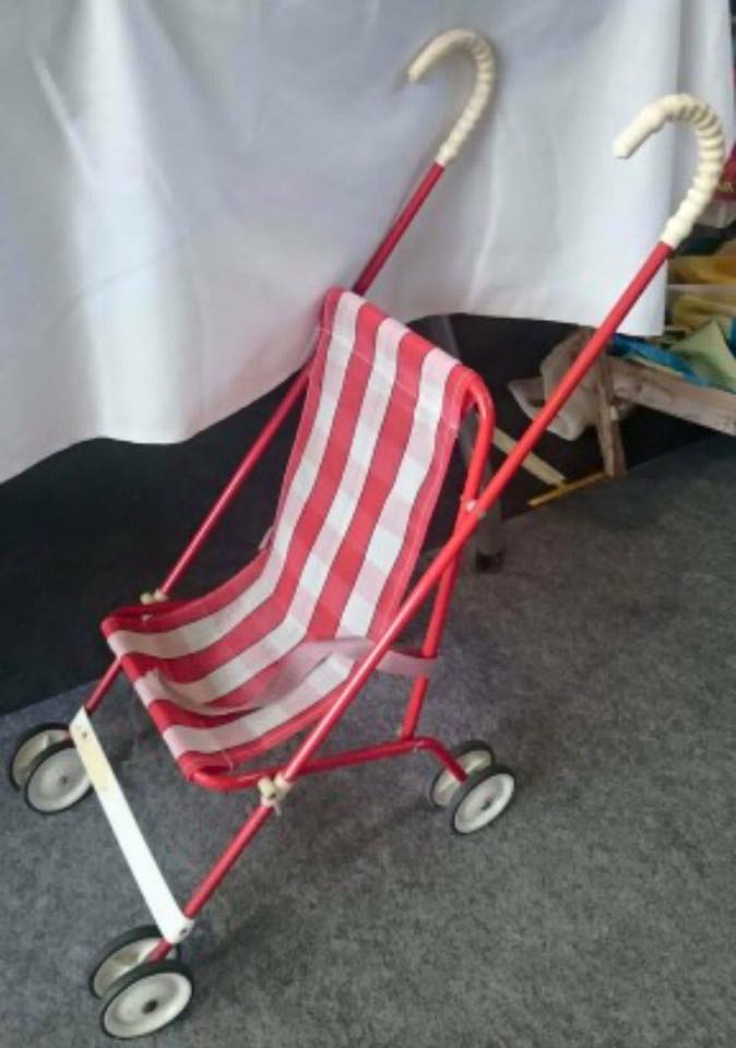 Silla de paseo de juguete con tela de rayas rojas y blancas.