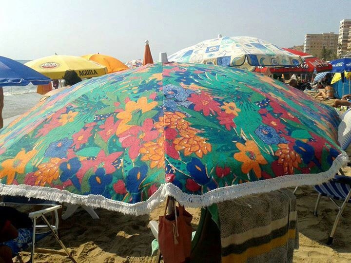Sombrilla de flores de colores en una playa llena de gente.