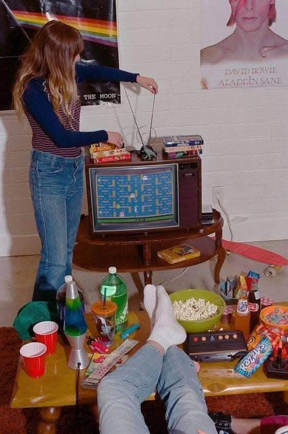 Chica jugando a una videoconsola conectada a una tele con refrescos y palomitas en la mesa