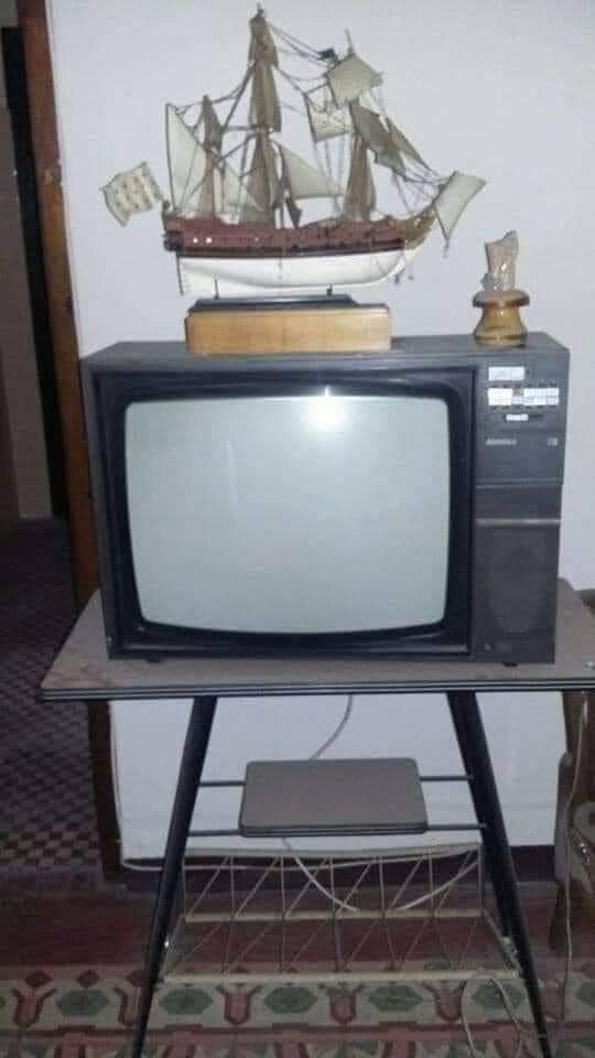 Televisor antiguo sobre una mesa con un barco de adorno encima