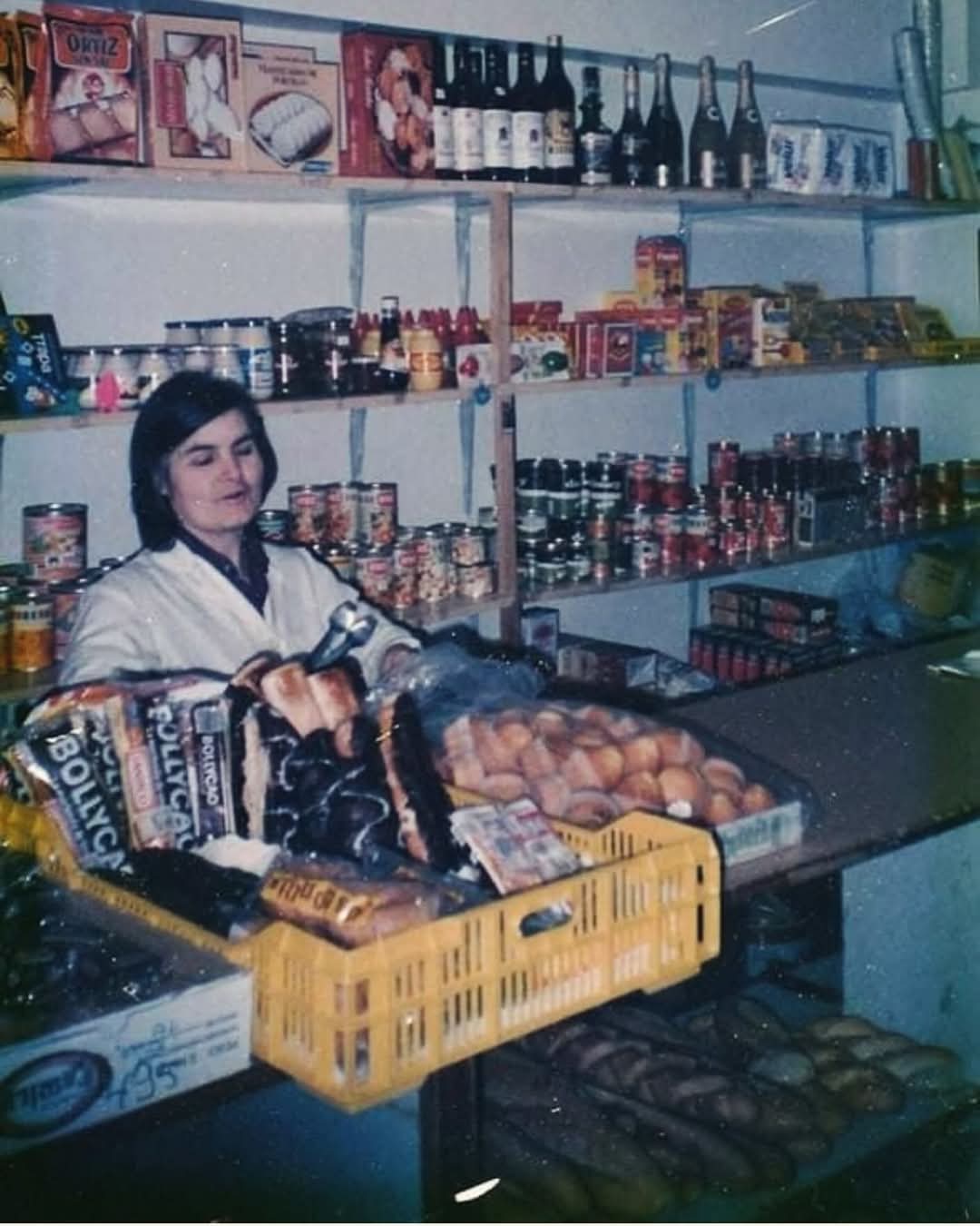 Dependienta en una tienda de comestibles con estanterías de latas y botellas