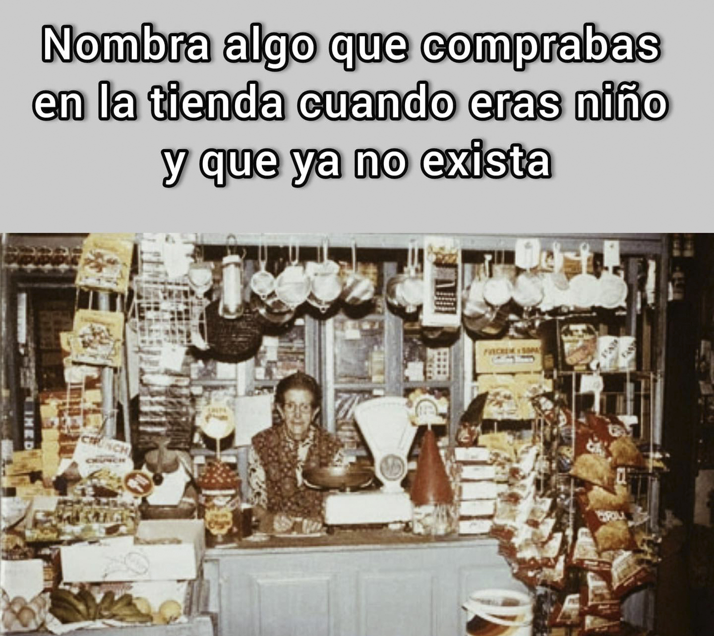 Tendera detrás del mostrador de una tienda antigua llena de cazos colgados, bolsas de patatas y una báscula.