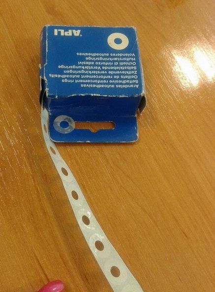 Caja azul de arandelas autoadhesivas APLI con una tira de arandelas blancas saliendo de ella.