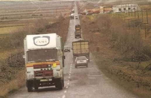 Camiones y coches circulando por una carretera nacional entre campos