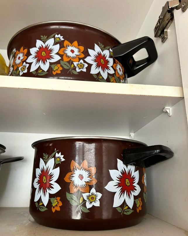 Dos cazuelas esmaltadas marrones con flores blancas y naranjas en un armario