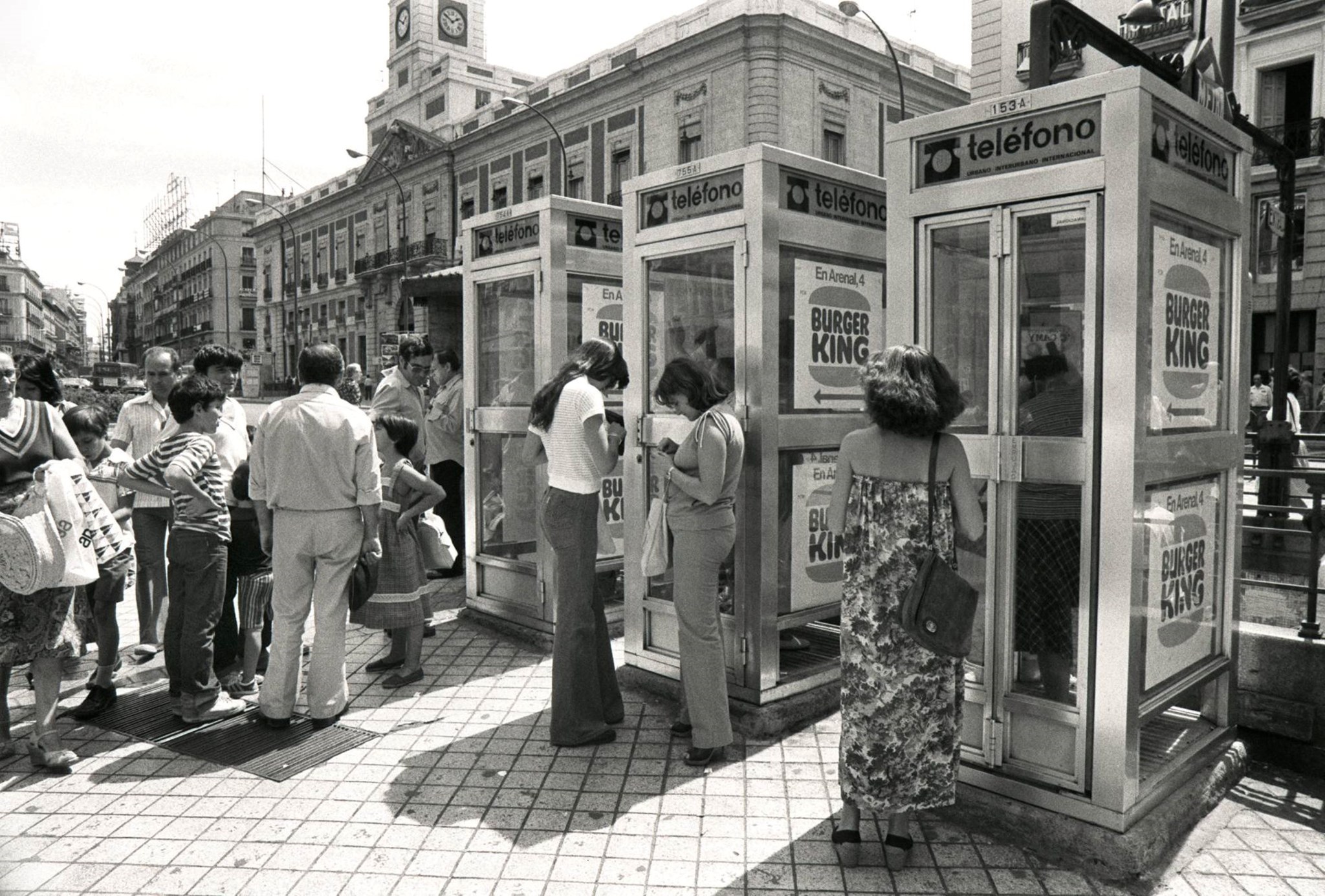 Gente haciendo cola junto a varias cabinas telefónicas en una plaza