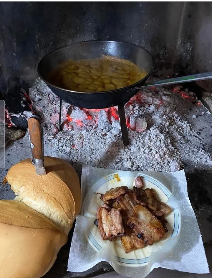 Sartén con patatas sobre brasas junto a pan y carne asada