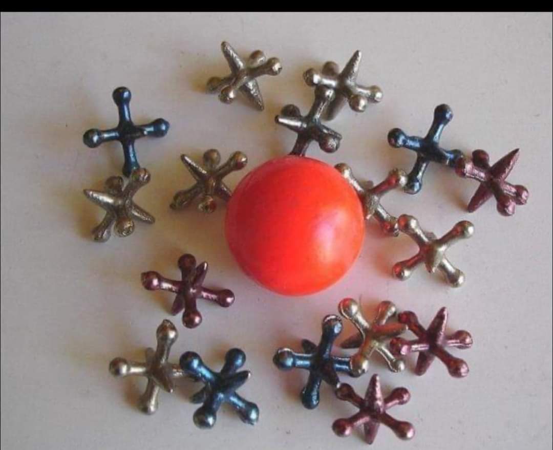 Piezas metálicas de colores con seis puntas alrededor de una pelota naranja de goma.