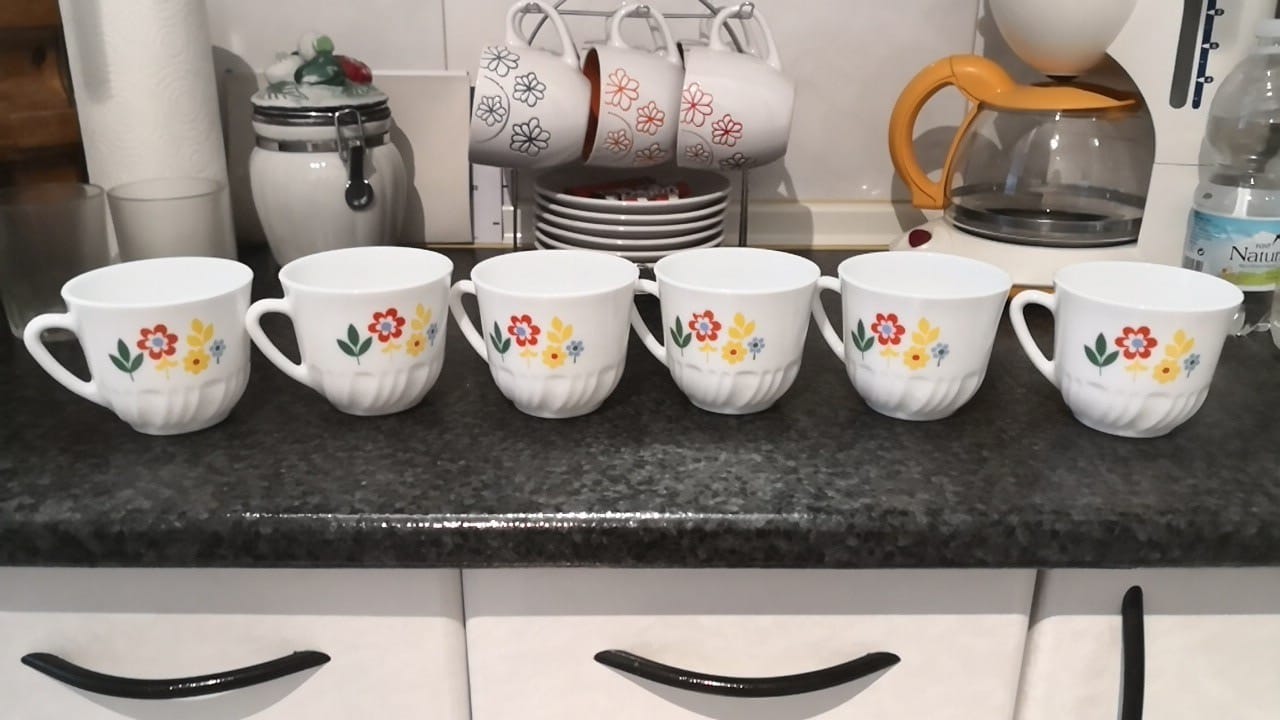 Seis tazas blancas con flores rojas y amarillas en una encimera.