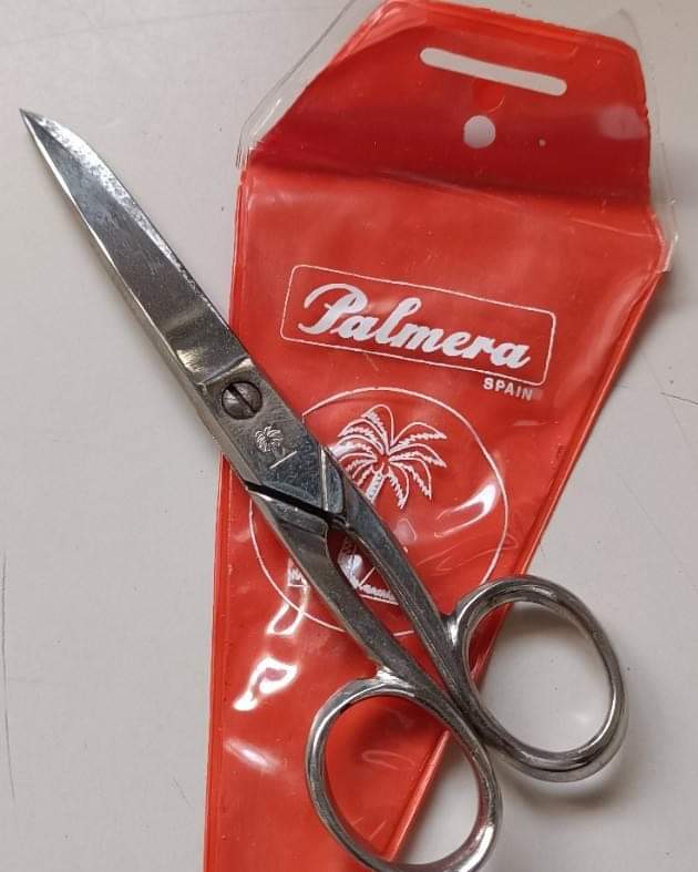 Tijeras de acero sobre una funda de plástico rojo con el logotipo de Palmera y una palmera dibujada.