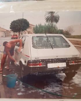Hombre lavando un coche blanco en la calle.