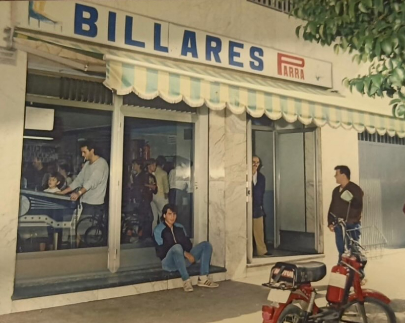 Fachada de un local de billares con gente en la puerta y una moto