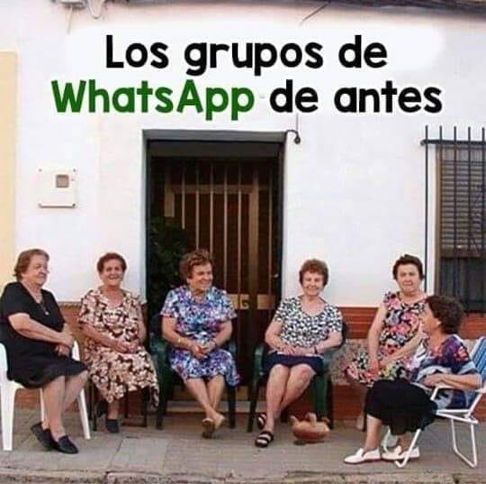 Seis mujeres mayores sentadas en sillas a la puerta de una casa blanca.