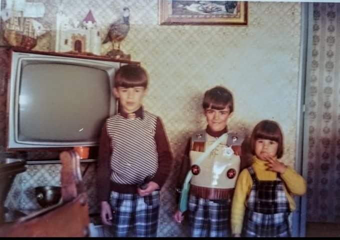 Tres niños posando junto a un televisor