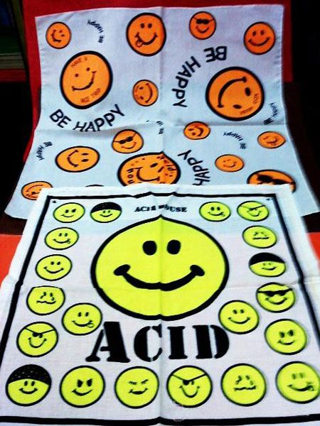 Dos pañuelos estampados con caras sonrientes amarillas y naranjas y las palabras Be happy y Acid.