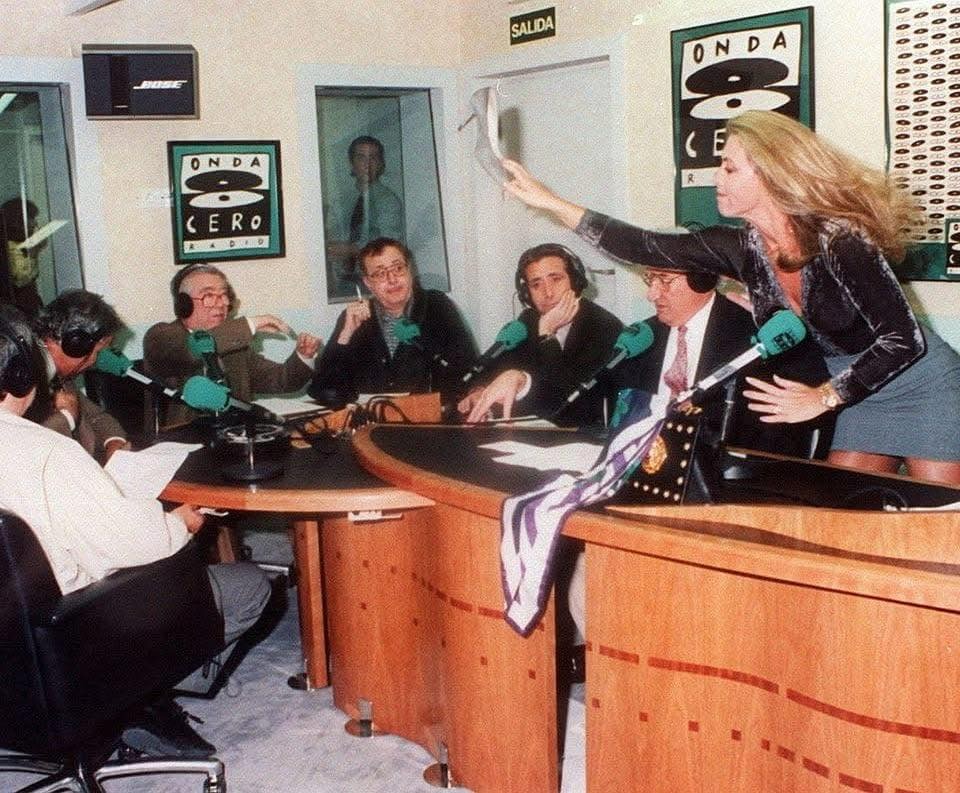 Mujer de pie sobre la mesa de un estudio de radio de Onda Cero ante varios locutores
