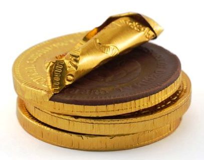 Monedas de chocolate apiladas, una a medio desenvolver.