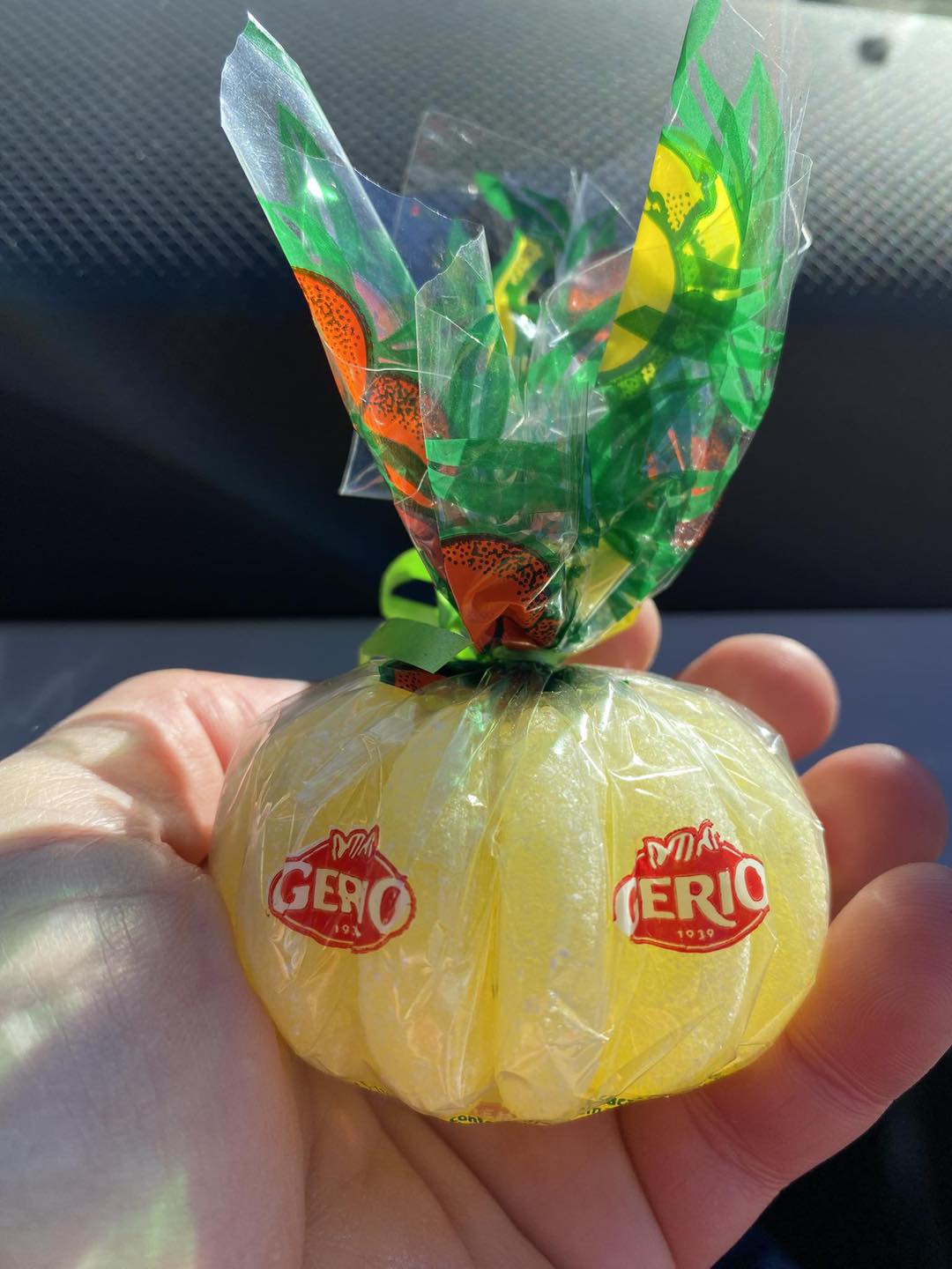 Mano que sostiene una naranja de caramelo Gerio envuelta en celofán.