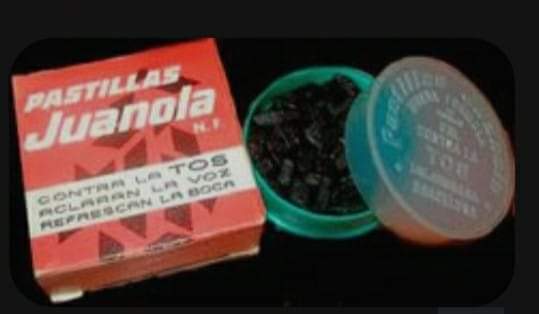 Caja roja de pastillas Juanola junto a una cajita redonda abierta con pastillas negras.