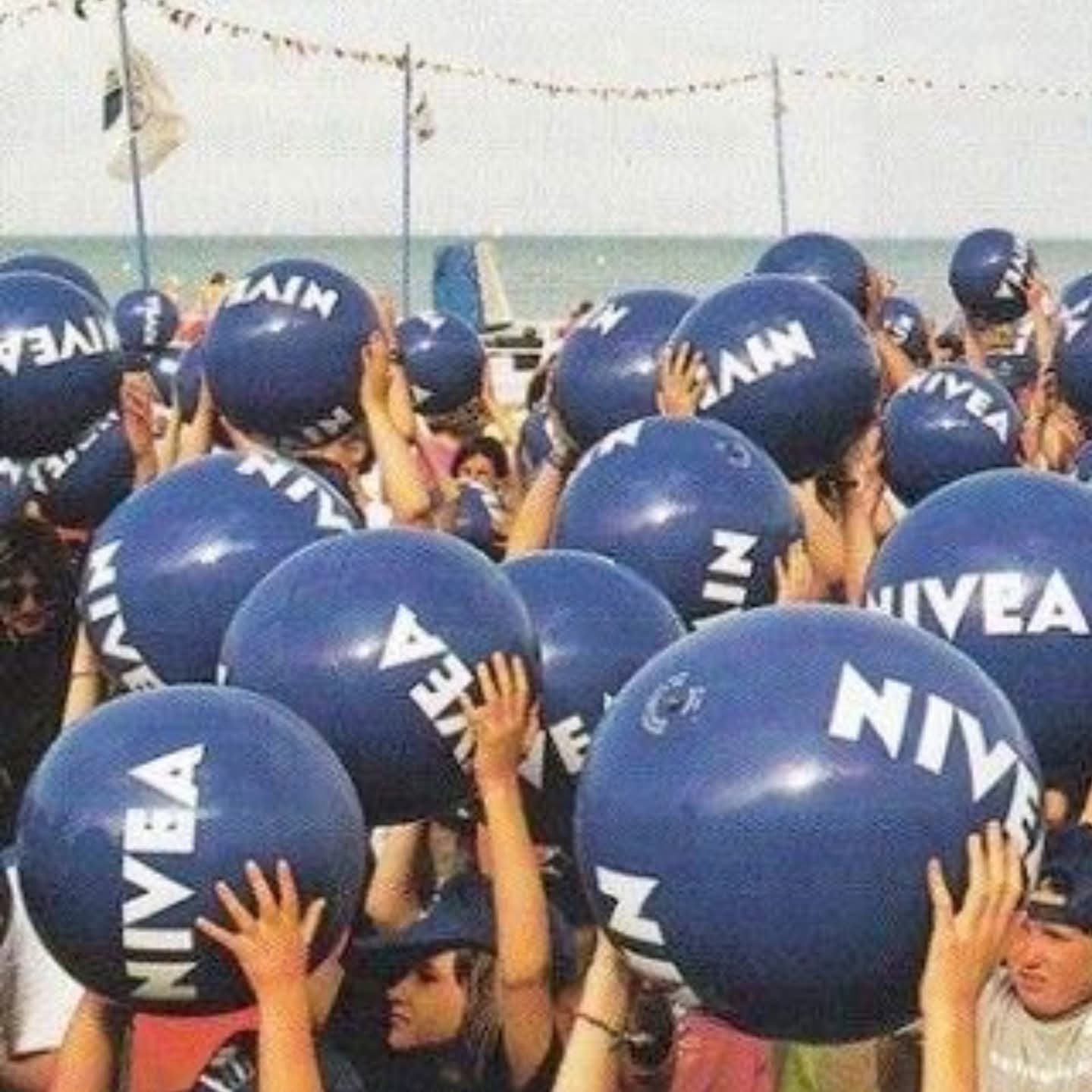 Multitud en la playa levantando pelotas azules de Nivea.