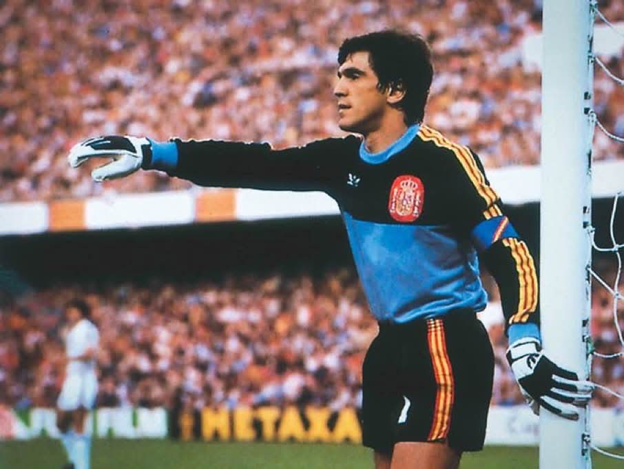 Portero de la selección española con jersey azul y negro señalando con la mano junto al poste de la portería.