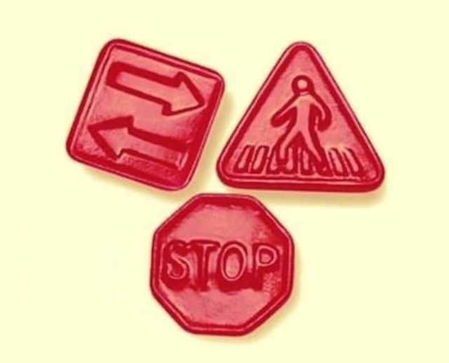 Tres gominolas rojas con forma de señales de tráfico: stop, paso de peatones y doble sentido.