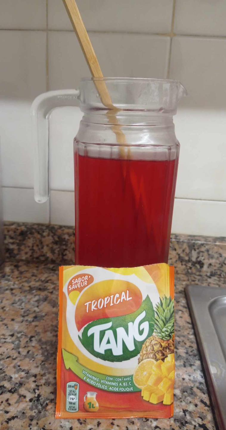 Jarra de cristal con refresco rojo y un sobre de Tang tropical delante.