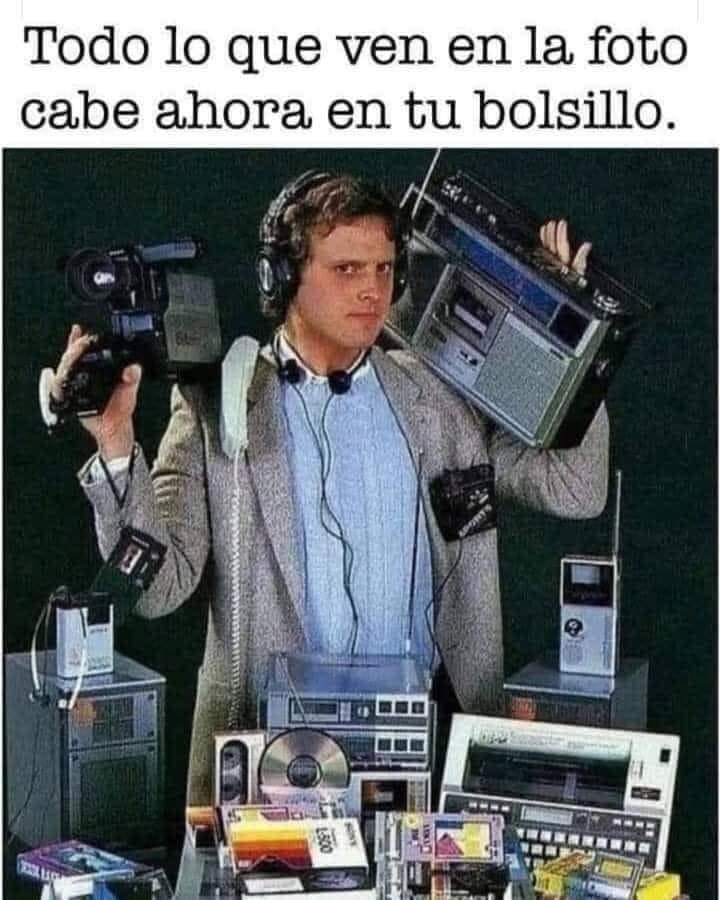 Hombre con americana cargando una videocámara, un radiocasete al hombro, cascos y muchos aparatos electrónicos de los años 80 alrededor.