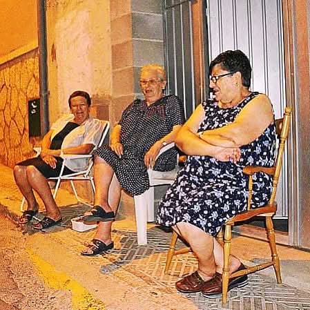 Tres mujeres mayores sentadas en sillas en la puerta de casa por la noche
