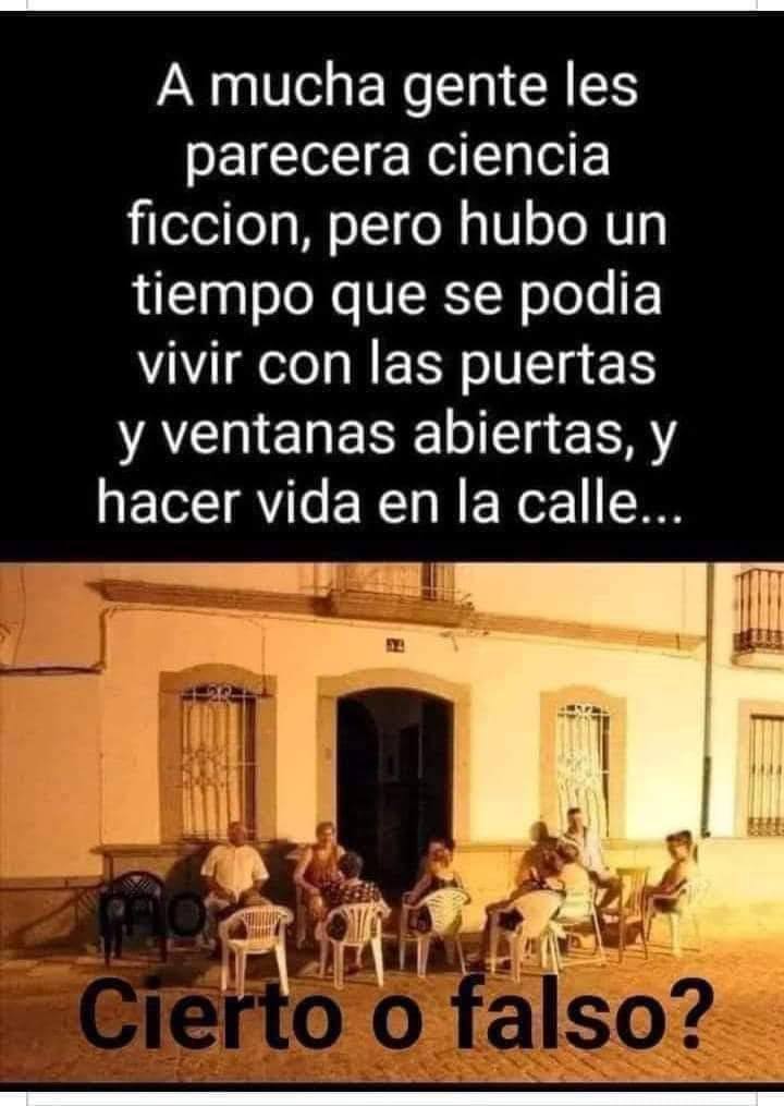 Grupo de vecinos sentados en sillas de plástico por la noche delante de una casa blanca con rejas.