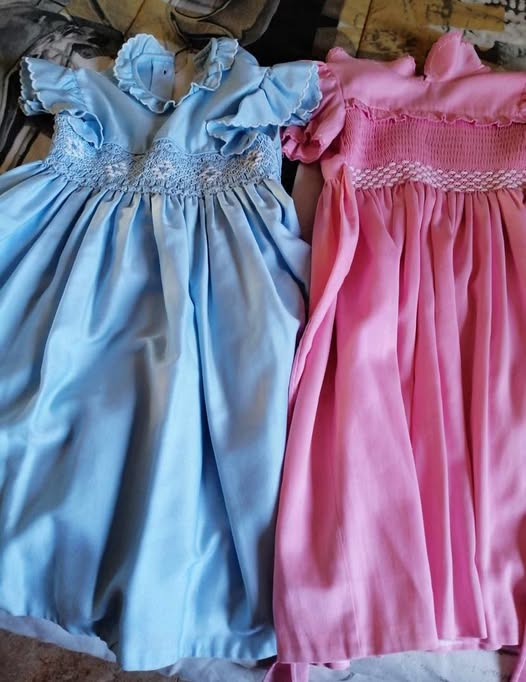Dos vestidos de niña, uno azul y otro rosa, con nido de abeja.