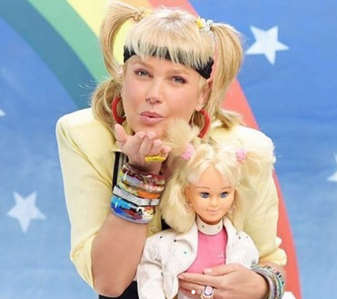 La presentadora Xuxa con coletas y una muñeca en un decorado de colores